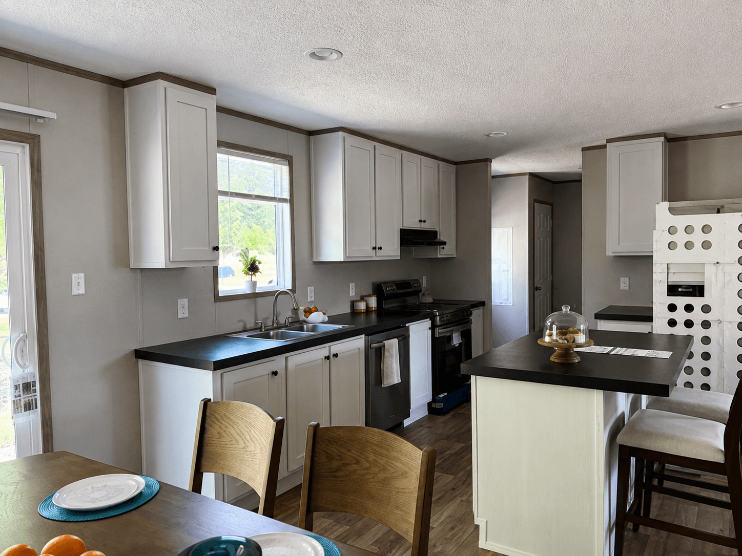 Compact kitchen with white shaker cabinets, black counters, a small island and a wood dining table in front