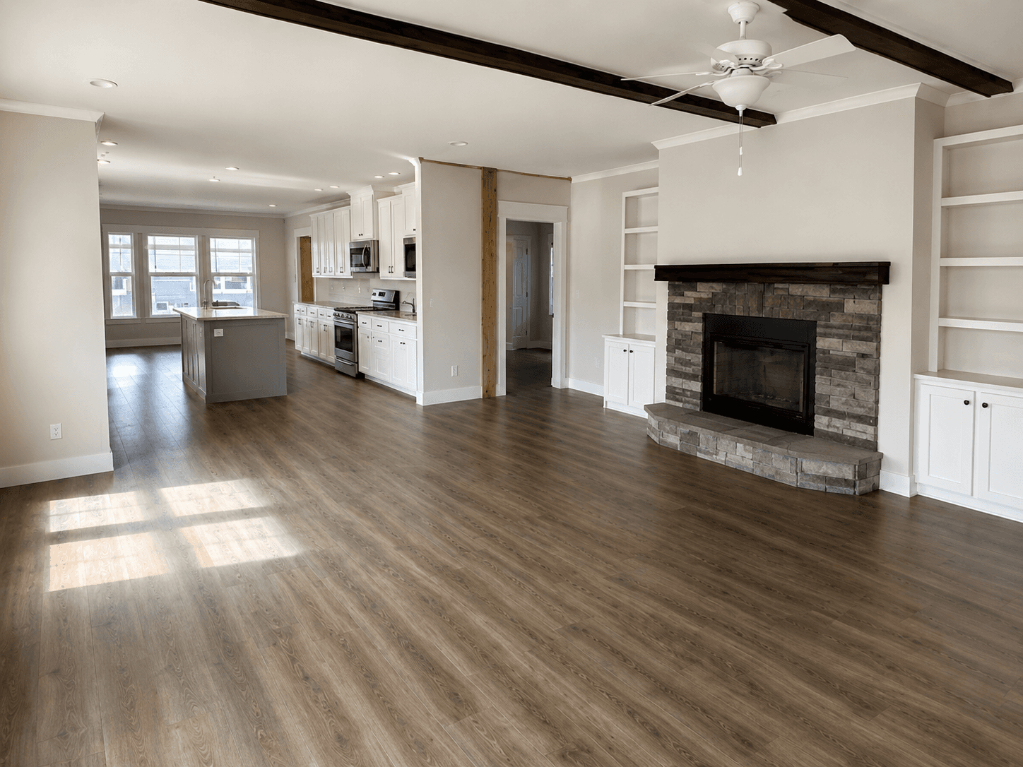 Great room with a stacked-stone fireplace, white built-ins, wood beams and a kitchen island beyond
