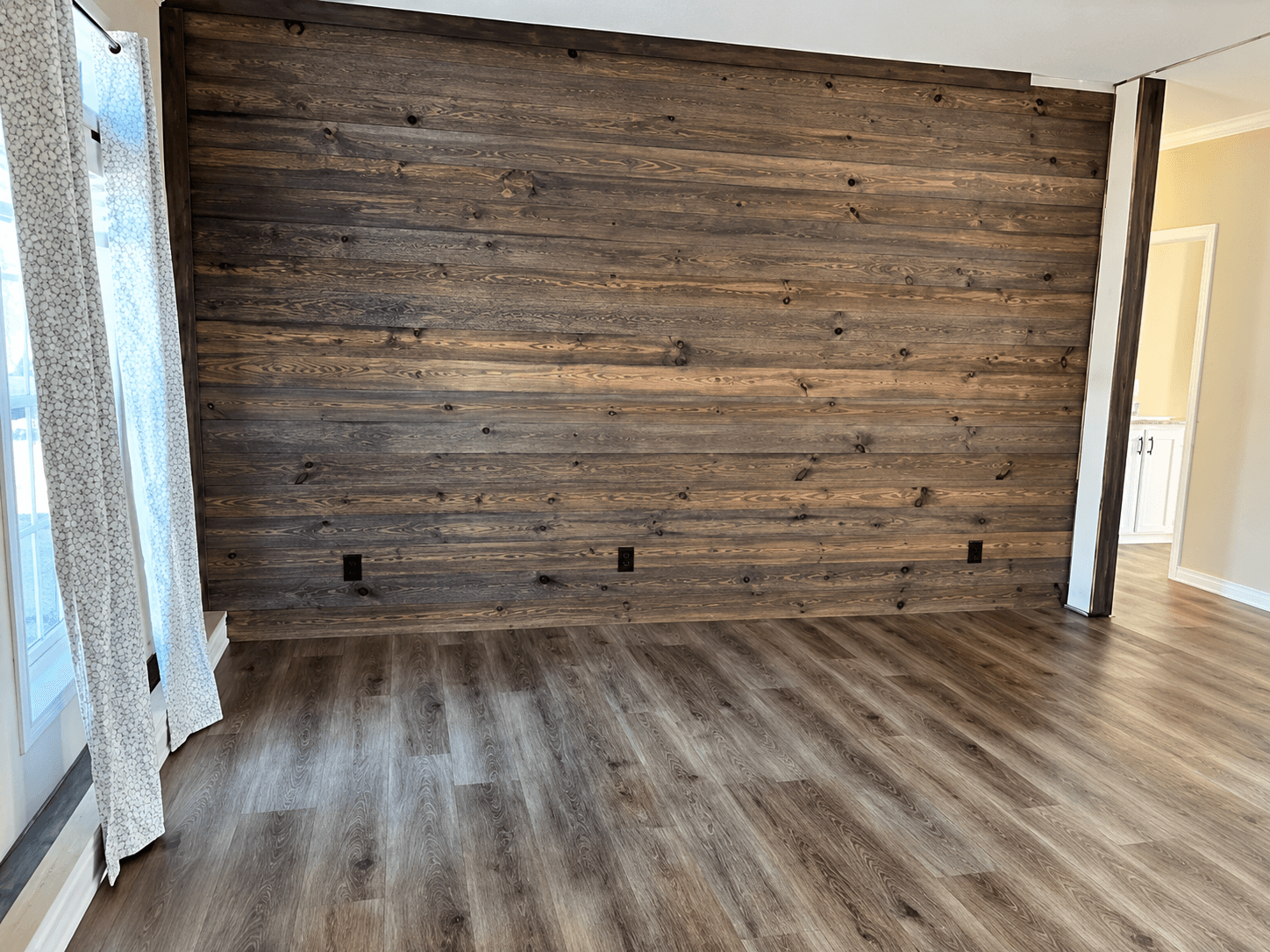 Empty room with a dark horizontal wood accent wall, wood-look flooring and patterned drapes
