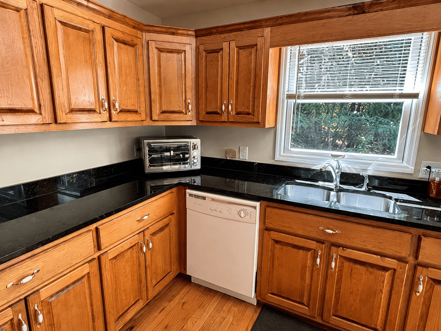 Kitchen with honey oak cabinets, a black countertop, white dishwasher and a window over the sink