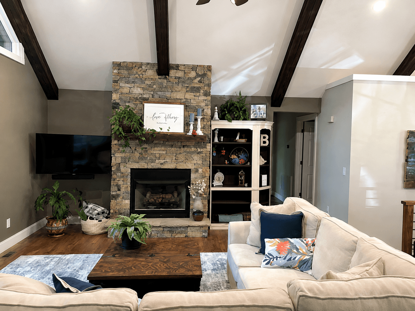 Living room with a stacked-stone fireplace, vaulted wood beams, a light sectional and a navy pillow