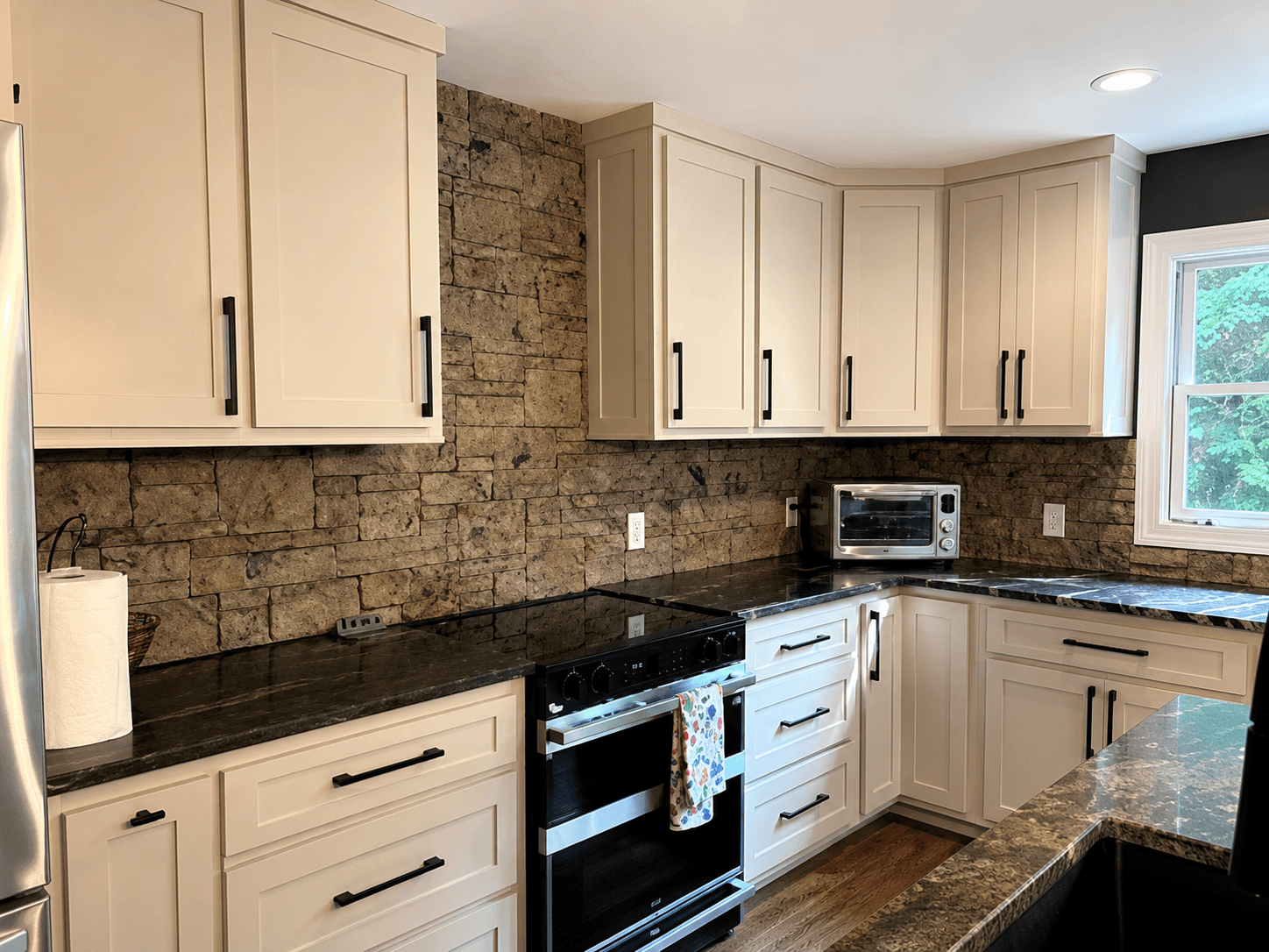 Kitchen with cream shaker cabinets, black hardware, a veined stone counter and a stacked-stone backsplash