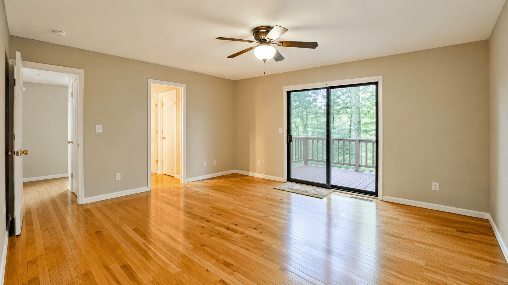 Empty bedroom with beige walls, hardwood floors, a ceiling fan and a sliding door to a wood deck