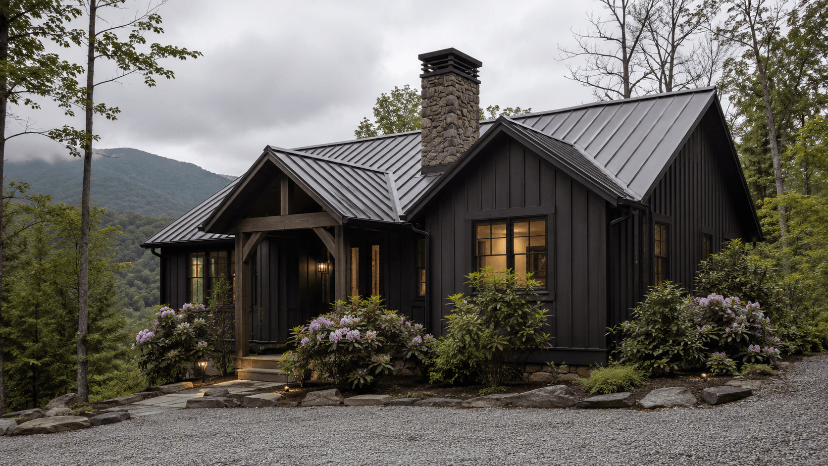 Dark board-and-batten cabin with a metal roof, stone chimney and rhododendron