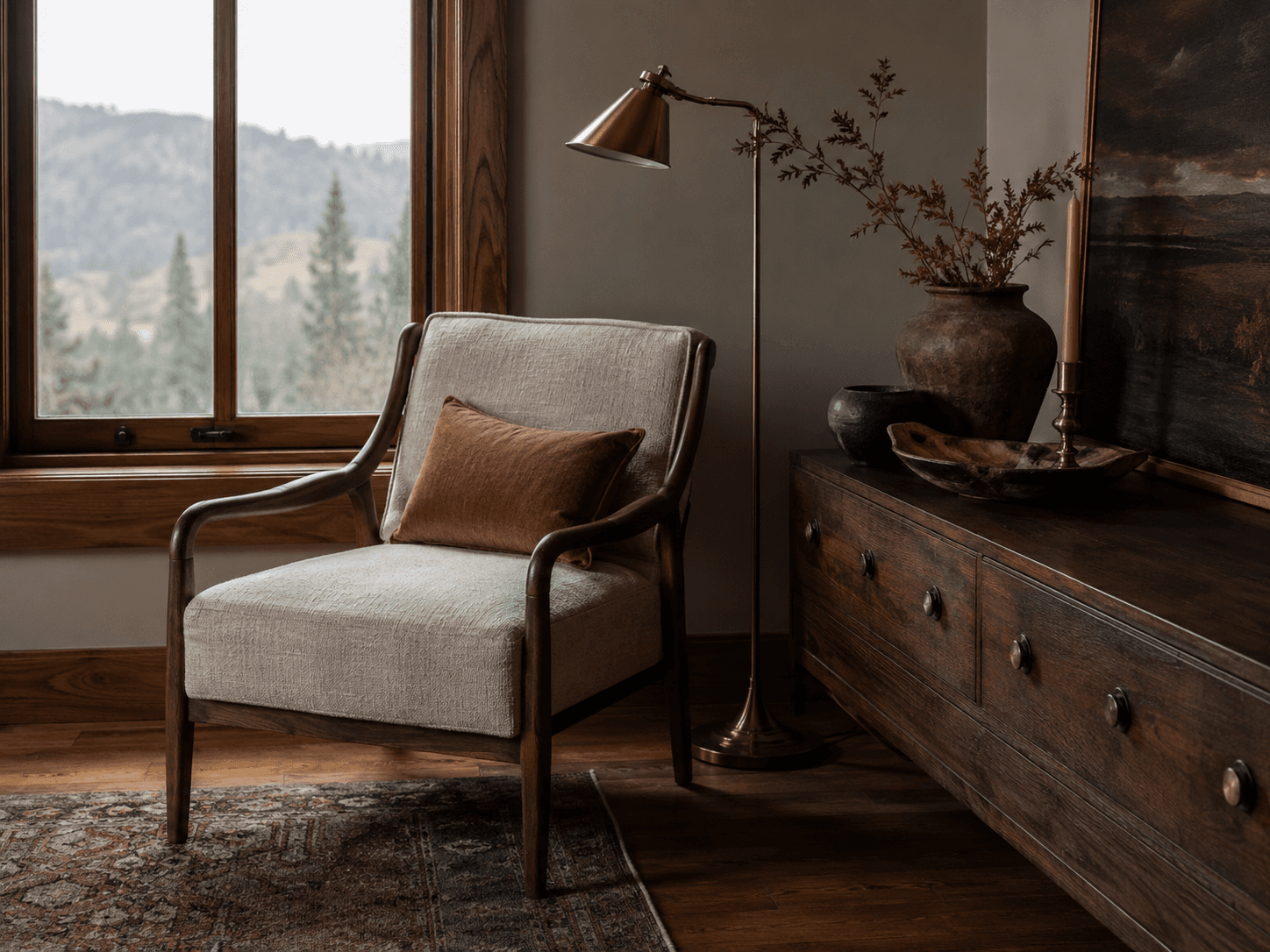 Linen armchair, brass lamp and ceramic vessels beside a mountain window