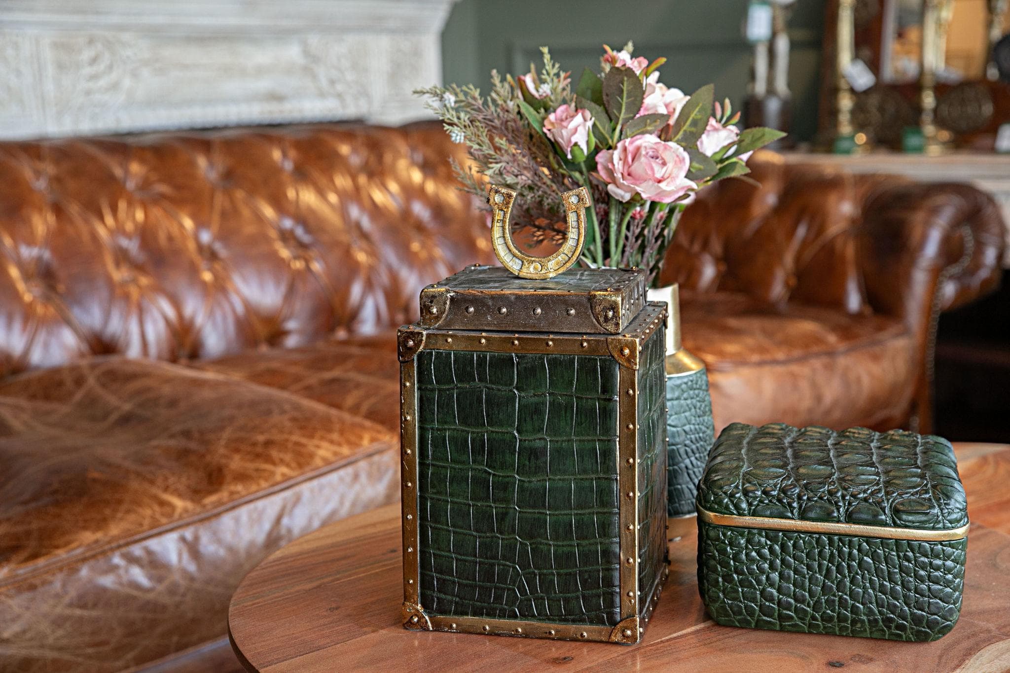 Decorative boxes and a floral arrangement styled on a wood table in front of a leather sofa