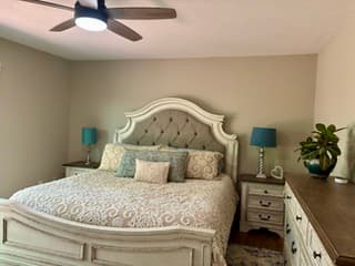 Bedroom with a tufted cream headboard, white nightstands, teal lampshades and a leafy plant