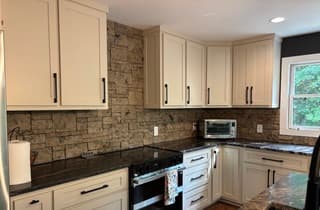 Kitchen with cream shaker cabinets, black hardware, a veined stone counter and a stacked-stone backsplash